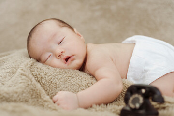 close-up photo of face of an Asian newborn sleeping happily on a brown carpet.