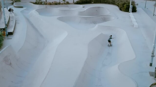 Drone shot of skateboarder ride inside modern smooth skateboard pool. Longboard or skating trick performance. Carving and bowl riding. Skater with flow