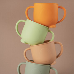 Modern colorful pastel silicone cups stacked in column on brown background. Baby tableware, first...
