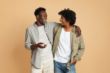 Two Cheerful Black Male Friends Embracing And Laughing On Beige Background