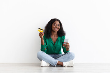 Cheerful african american woman holding credit card and cellphone
