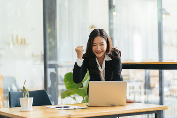 Excited young woman standing at table with laptop and celebrating success