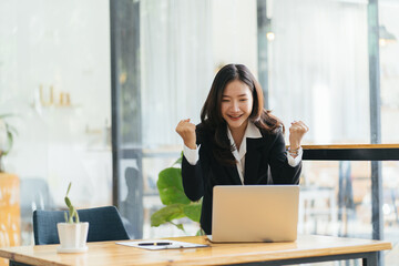 Excited young woman standing at table with laptop and celebrating success
