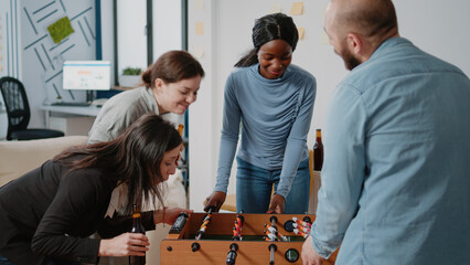 Diverse group of people enjoying fun activity after work with foosball game table and drinks....