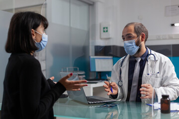 Obraz premium Specialist and person discussing about health at checkup appointment in cabinet. Medic talking to woman about prescription medicine and treatment during coronavirus pandemic. Medical visit