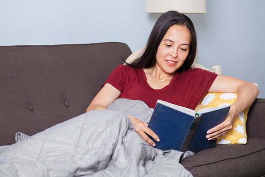 Woman reads on couch with weighted blanket