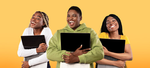 Tech Lovers Concept. Joyful Black Women Embracing Laptops With Blank Screens