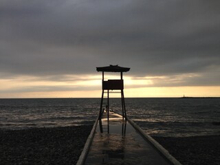 Beach lifeguard post at the sunset.  Lifeguard tower on the stone pier in front of calm sea at the sunset. Rescue. Safety. Water. Measurement. Prevention. Aid. Assistance. Rescuers