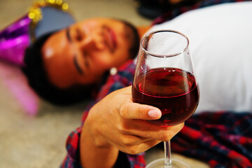 Man drunk with wine lying on the floor, drunken sleep on the floor, holding a glass of wine.