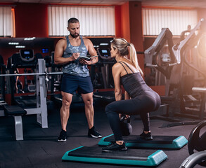 Personal trainer helping young woman on her work out in gym. kettlebell squats