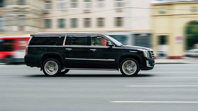 Fast moving Cadillac Escalade ESV on the city road. Black SUV with man driving. Premium auto in fast motion with blurred background. Speeding in the city concept