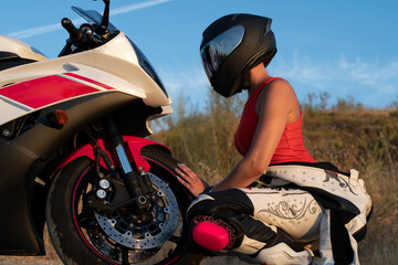 Fototapeta na wymiar young woman dressed as a biker with a safety helmet crouching down and leaning on the front wheel of her road motorcycle