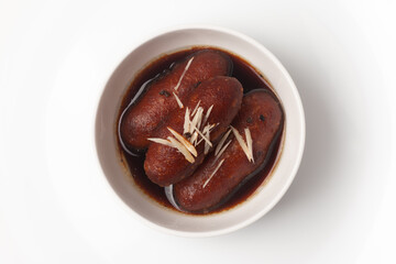 Close-up of Indian Bangali traditional sweet dish Pitha or Peetha ( Roshopuli ) made from red sweet potato, garnished with chopped almond and dry nuts with cardamom dipped into sugar syrup 