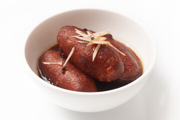 Close-up of Indian Bangali traditional sweet dish Pitha or Peetha ( Roshopuli ) made from red sweet potato, garnished with chopped almond and dry nuts with cardamom dipped into sugar syrup
