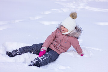 Fototapeta na wymiar Cute little girl lies in a snowdrift and smile.