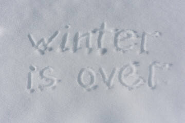 Inscription Winter is over, written on white surface of the snow. Top view. Flat lay. Winter holiday concept. Sunlight.