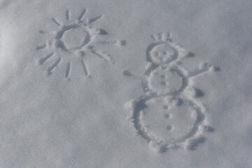 Fototapeta na wymiar A snowman and the sun drawn with a finger on a white fluffy surface of snow. Top view. Flat lay. Text space on the left.