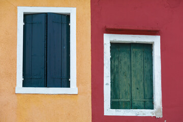 Fototapeta na wymiar Old walls of red and orange with the windows closed shutters, Burano, Venice