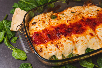 Vegetarian cannelloni or lasagna with spinach close up, tomato sauce, bachamel and cheese on a black background. Traditional homemade classic italian cuisine concept.