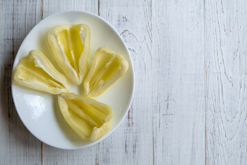 Cut in half yellow bell peppers on a white plate on a light wooden background.