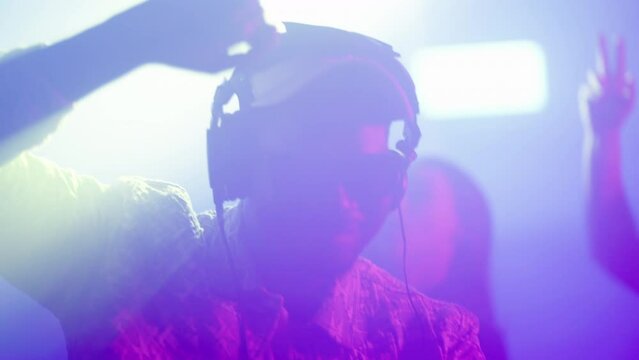 African man with sunglasses and headphones enjoying party in music club. View against light. Nightlife, modern music and entertainment concept.