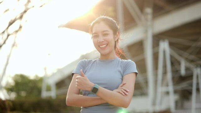 Portrait young beautiful asian woman wearing smart watch and standing pose smiling in the city at sunrise. Cheerfully sporty female workout and exercise wearing sport wear in the morning.