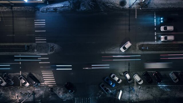 Traffic in the night city is long traces of car headlights. Time-lapse of night intersection - headlight lights at long shutter speed from cars. Top view Drone shot.