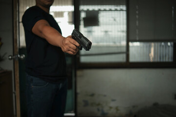 Man holding a pistol, standing in a room in black, pointing and aiming a gun at a target. concept...