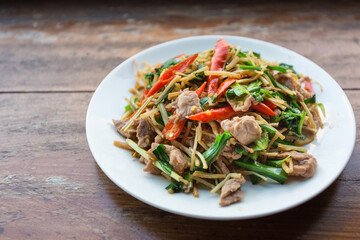 Pork with garlic chives (long root) is one of traditional Akha’s food in Northern of Thailand. It put on a white plate on a wooden table.