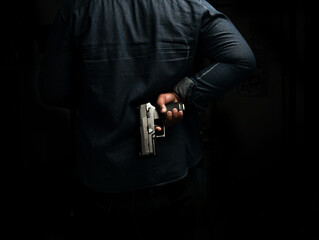 A man in a blue denim shirt is standing in a dark room with a pistol behind him. concept of...