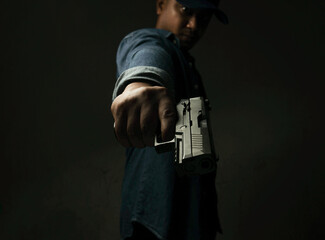 A man in a blue denim shirt is standing in a dark room with a pistol. Point and aim the gun at the target. concept of assassination, murder, criminal