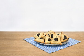 Triangular cookies with poppy seeds ( hamantasch or aman ears ) on plate on wooden table on light background with space for text. For purim celebration