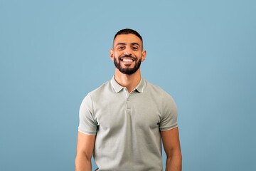 Portrait of happy arabic guy smiling at camera over blue studio background, showing positive...