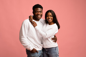 Fototapeta premium Cheerful young black lovers embracing on pink