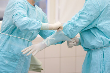 Оne pair of hands puts the surgeon's gloves on the other pair of hands