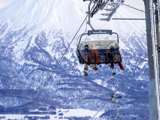Fototapeta na wymiar Chairlift with a snowy volcano in background (Niseko, Hokkaido, Japan)