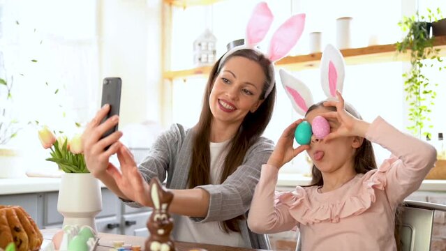 Mother and daughter doing selfie with Easter eggs, wearing bunny ears, have beauty and fun day together at home. Concept of childhood, happiness, family's weekend, friendship party. Domestic lifestyle