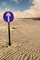Direction sign on a empty beach to Omey island at low tide. Transportation. County Galway, Ireland. Vertical image.