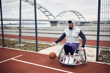 Athletic man in wheelchair comes to basketball practice on outdoor court.