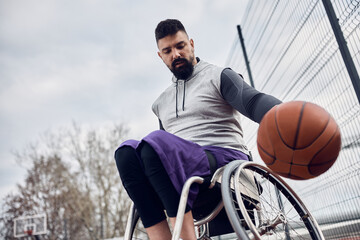 Fototapeta premium Young athletic man in wheelchair exercising basketball outdoors.