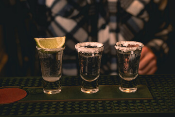 Three tequila shot rimmed with salt served with lime on bar counter