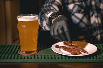 Glass of beer standing on bar counter while bartender putting dried meat on plate