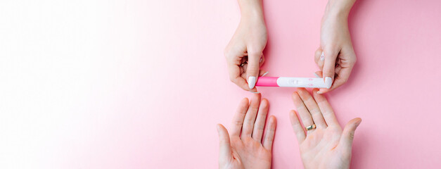 Pregnancy test happy. Female hand hold positive pregnant test with silk ribbon on pink banner...