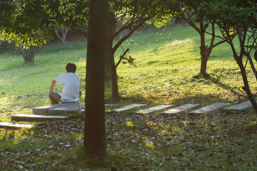 Asian man seating alone in green nature, next to trees and grass