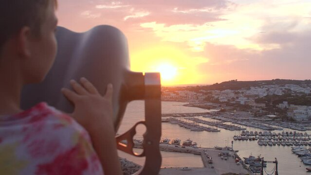 A child looks at the sea and skyline with the mechanical binocular vending machine. Coin operated binoculars at a tourist destination as travel. 8.10.2021 Santa Maria di Leuca, Lecce, Italy. 