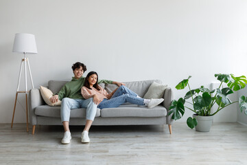 Affectionate young Asian couple cuddling on couch in living room, spending time together, free space