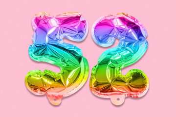 Rainbow foil balloon number, digit fifty two on a pink background. Birthday greeting card with...