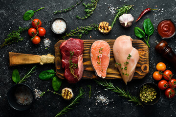 A set of different meats: salmon steak, beef steak and chicken breast. On a black stone background.