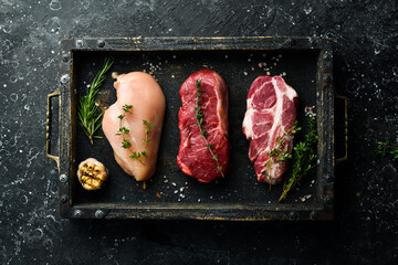 Meat: beef steak, chicken breast and pork. Ready to cook. Top view. On a black stone background.