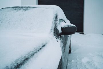 Car covered in snow near the garage and snow in the background